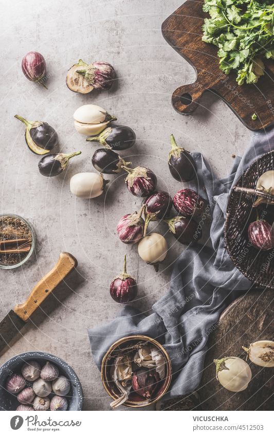 Kochen mit Auberginen: lila und gestreifte Auberginen auf dem Küchentisch mit Geschirrtuch, Messer, Schneidebrett und Knoblauch. Gesundes Kochen zu Hause mit Sommergemüse der Saison. Ansicht von oben.