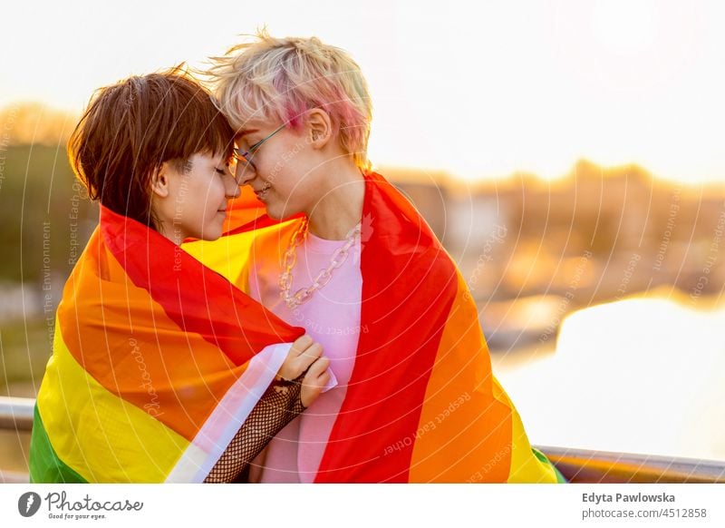 Junges nicht-binäres Liebespaar, das sich unter einer Regenbogenflagge umarmt Homosexuelles Paar Zusammensein romantisch queer geschlechtsfluid lgbt