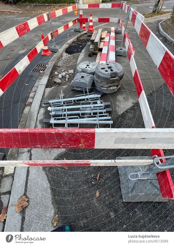 Tiefbau-Baustelle. Ein kleines Teilstück eines Bürgersteigs wird repariert. Er ist von einer Baustellenabsperrung aus rot-weißen Brettern umgeben. Es sind auch Baumaschinen vorhanden.