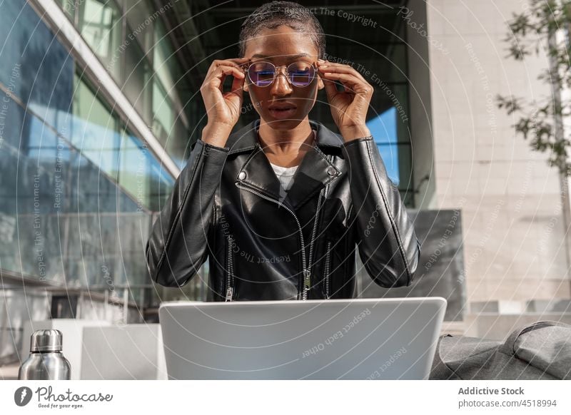 Schwarze Frau mit Thermoskanne und Laptop auf der Straße Browsen Heißgetränk online freiberuflich Getränk Großstadt Arbeit Netbook Apparatur trinken modern