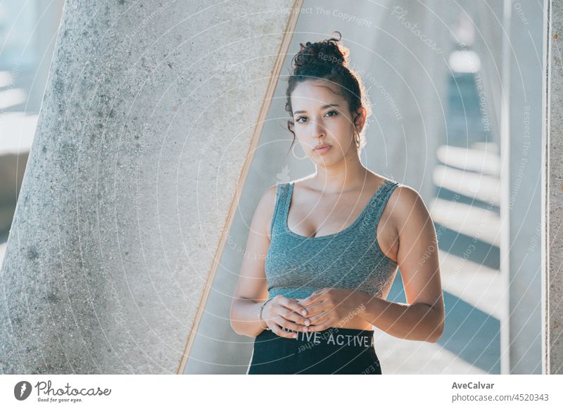 Junge afrikanische Frau, die während eines Sonnenuntergangs in der Stadt auf Sportkleidung in die Kamera schaut, Betonhintergrund, städtischer Sportstil, Kopierraum, junge Athleten