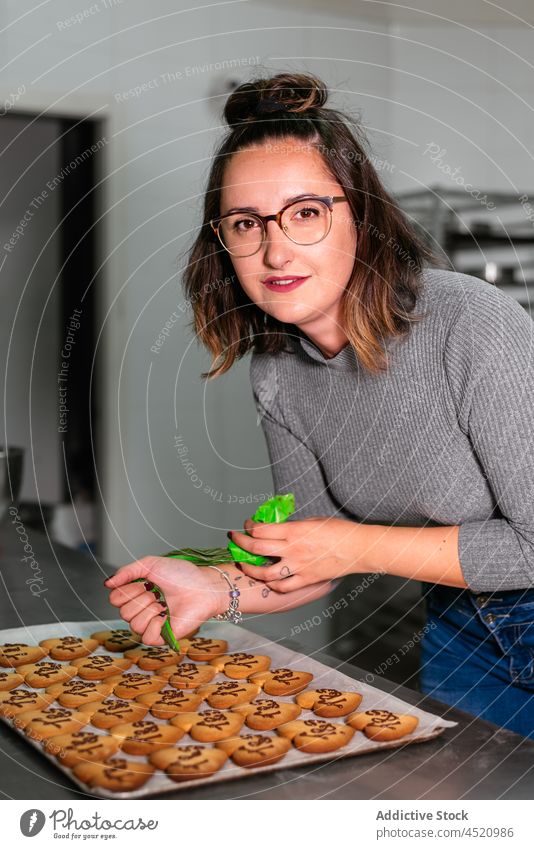 Konzentrierte Bäckerin beim Verzieren von Ingwerkeksen mit Schokoladenglasur Frau dekorieren Keks Konditor Bäckerei Dessert Backwarenbeutel Gebäck süß Herz