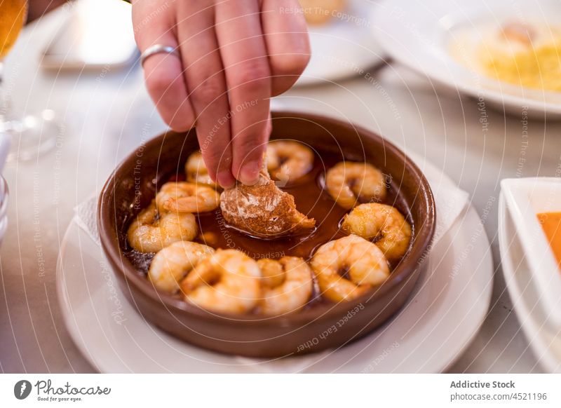 Gesichtslose Frau taucht Brot in die Soße eines Garnelengerichts Dip Saucen Granele Gambas al ajillo Meeresfrüchte Restaurant essen hungrig lecker Küche