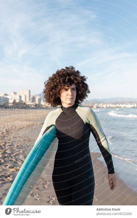 Lockenhaarige Frau mit Surfbrett am Meer Surfer Spaziergang MEER tropisch Strand winken schäumen sorgenfrei Aktivität Meeresufer Neoprenanzug Brandung Küste