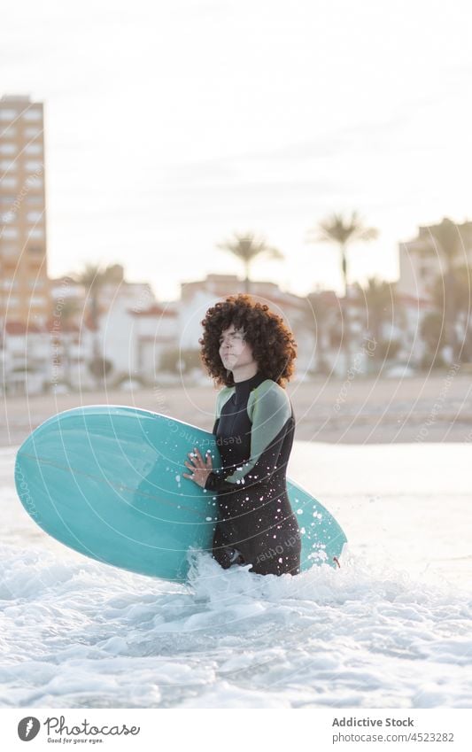 Lächelnde Frau im Neoprenanzug mit Surfbrett im wogenden Meer Surfer MEER winken genießen Strand sich[Akk] entspannen schäumen Küste Meerwasser Wasser platschen