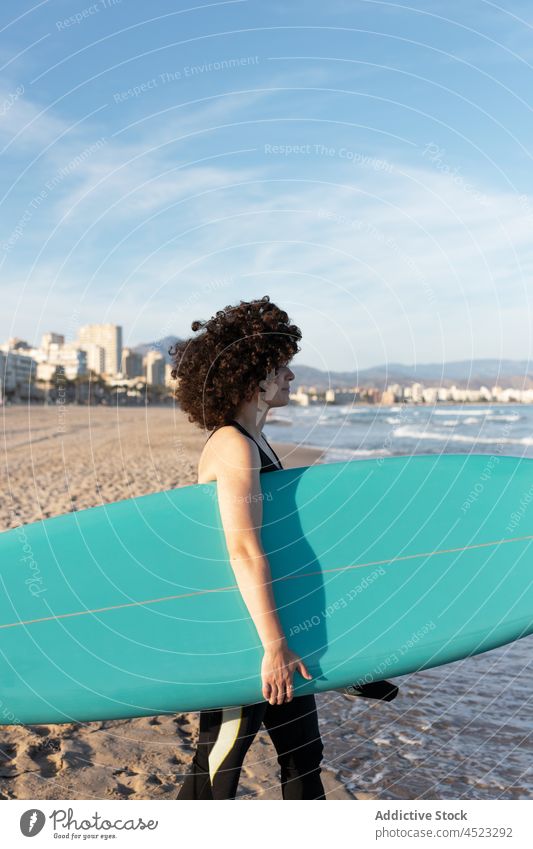 Lockenköpfige Frau mit Surfbrett am Meeresufer Surfer MEER tropisch Strand winken schäumen sorgenfrei Aktivität Neoprenanzug Brandung Küste Ufer Wasser