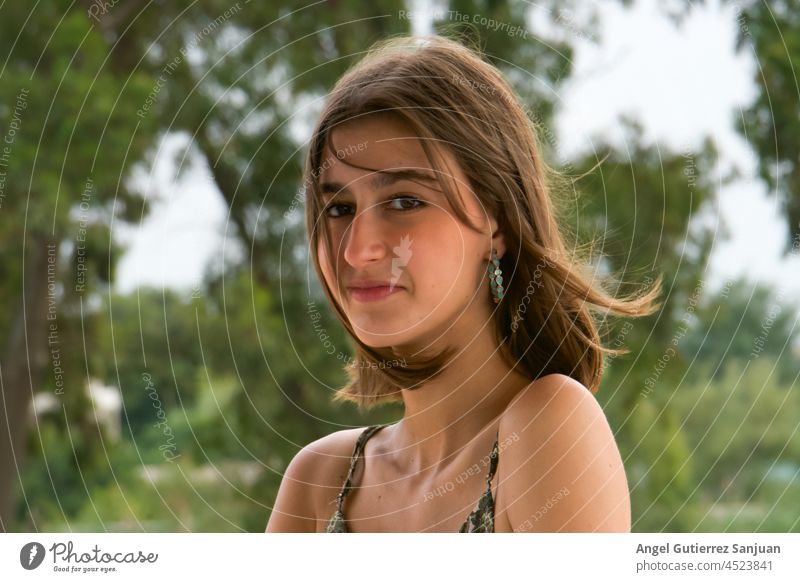 Junge brünette Frau schaut in die Kamera und lächelt, während sie vor einem natürlichen Hintergrund posiert. junger Erwachsener Pose Natur Hintergründe