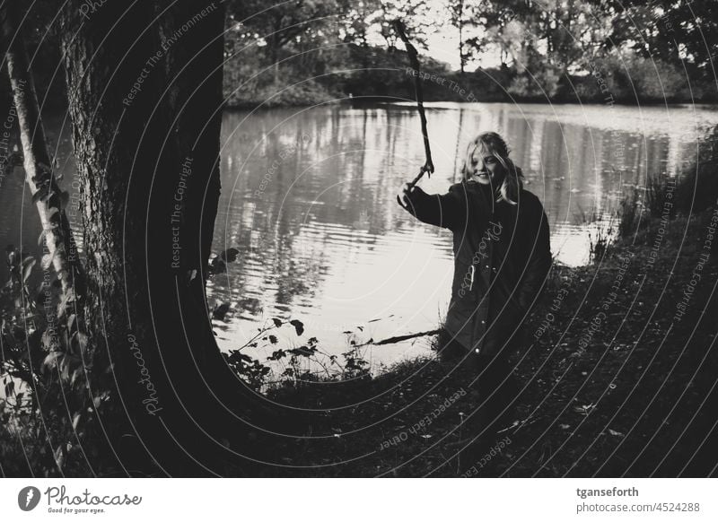 Kind mit einem Stock am Wasser Mädchen Herbst See spielen draußen draußensein draußen spielen Ast werfen Kindheit Natur Außenaufnahme Spielen Freude Glück