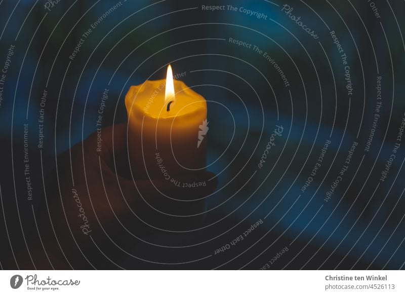 Brennende Kerze in einer Hand. Schwache Tiefenschärfe und blauer Hintergrund. Kerzenschein Licht Flamme dunkel leuchten schwache Tiefenschärfe