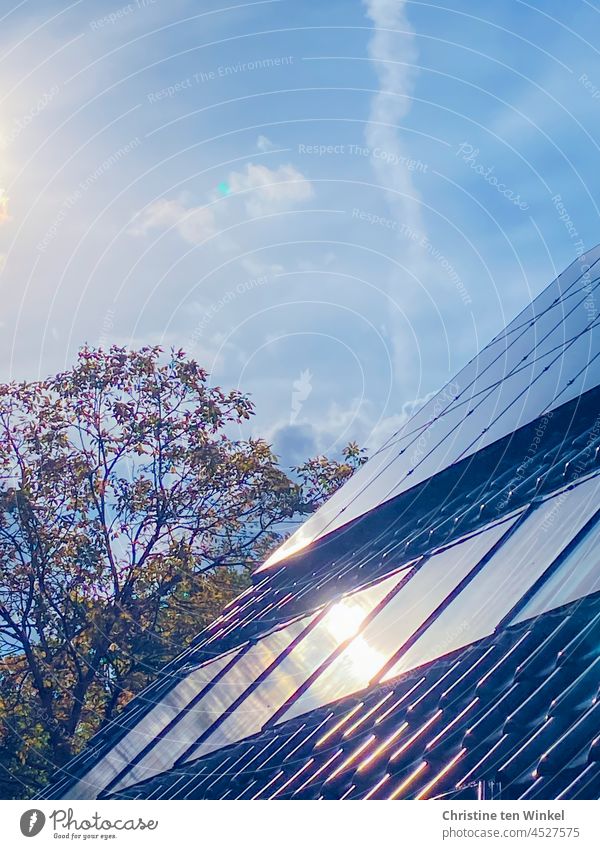 Die Sonne scheint hell vom leicht bewölkten Himmel und spiegelt sich in den Kollektoren der Solaranlage und der Photovoltaikanlage eines Wohnhauses Energiewende