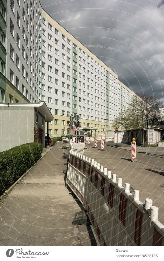 Straßenbau vor einer besonnten Plattenbaufassade unter bedecktem Himmel Gebäude Fassade Fenster Wohngebäude Bürgersteig Absperrung Baustelle Tiefbau