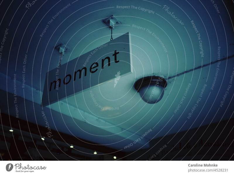 Schild mit der Aufschrift "Moment" hängt von einer Decke in einer Gasse Lampe Schilder & Markierungen Hinweisschild Menschenleer Schriftzeichen Außenaufnahme