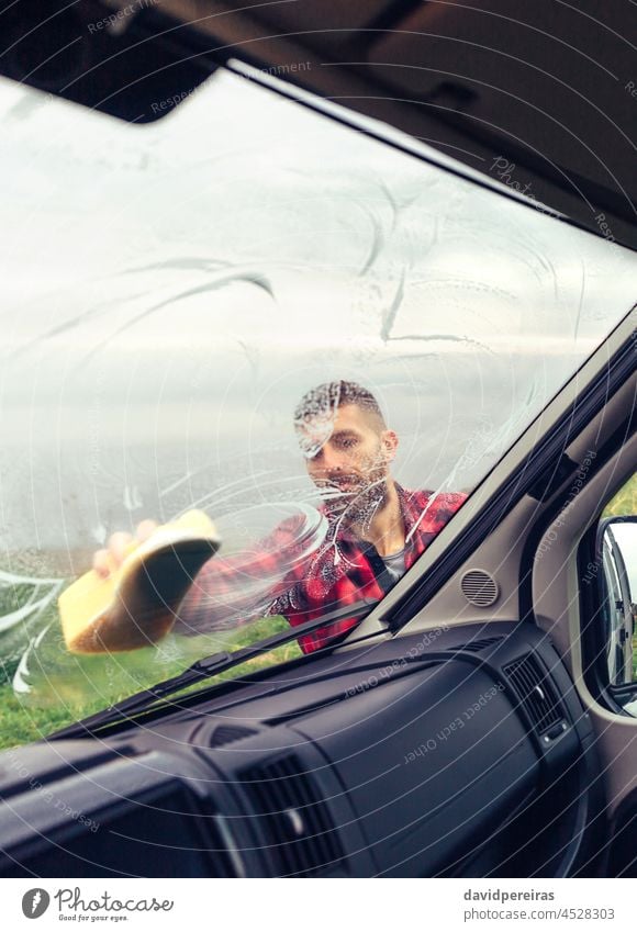 Mann reinigt Wohnmobilglas im Freien jung Reinigen einseifend Glas Fenster Schwamm Blick von innen durch das Glas Windschutzscheibe vorsichtig Besitzer