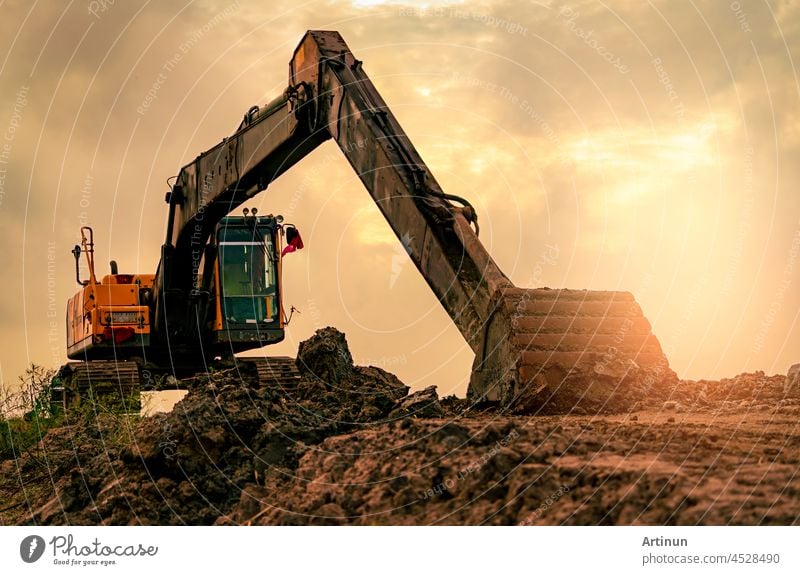 Bagger geparkt auf der Baustelle nach dem Graben Boden. Bulldozer auf Sonnenuntergang Himmel und Wolken Hintergrund. Bagger nach der Arbeit. Erdbewegungsmaschine auf der Baustelle in der Abenddämmerung. Bagger mit Schmutz Schaufel.