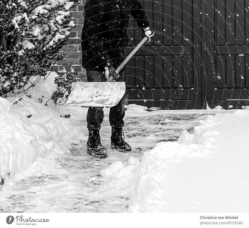 Ein Mann räumt Schnee vor seiner Garage, während es immer noch weiter schneit Schneeschippen Schneeschieben schnee schippen Schnee räumen Neuschnee schneien