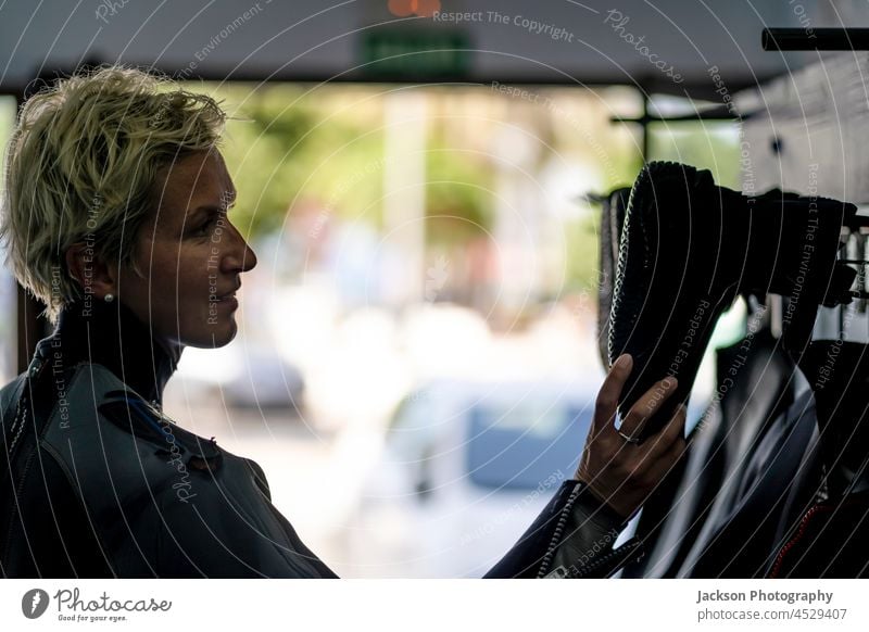 Blonde Frau im Neoprenanzug wählt Stiefel für Wasserabenteuer wählen Schuhe Werkstatt Kaukasier Erwachsener professionell Person Menschen Wassersport Gerät