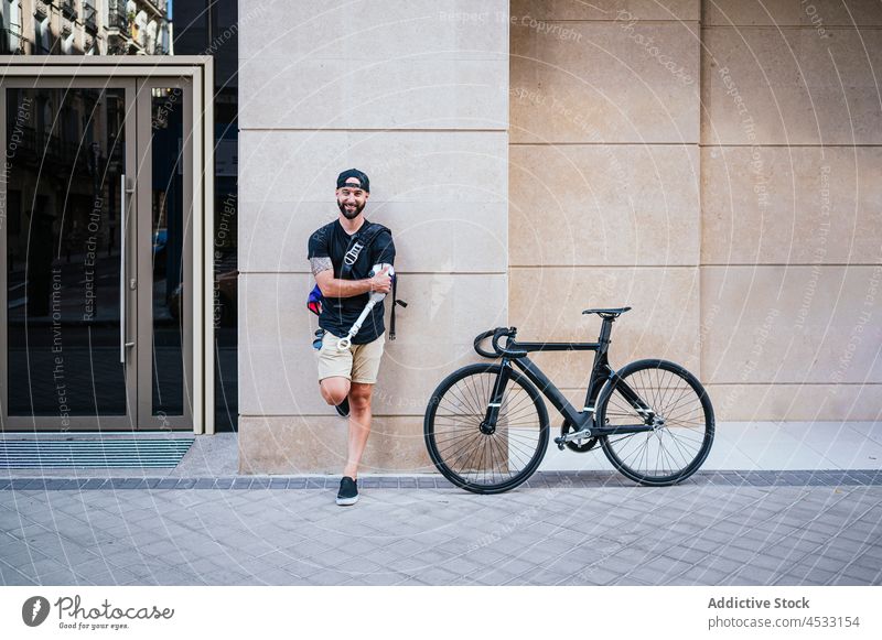 Lächelnder Mann mit Armprothese in der Stadt stehend Arme Prothesen Großstadt Hipster heiter deaktivieren Straße Amputierte Bionik männlich Handicap Fahrrad