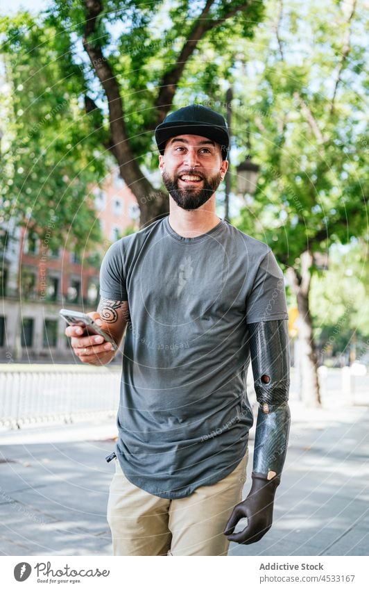 Fröhlicher Mann mit künstlichem Arm beim Surfen auf dem Smartphone Prothesen Arme Browsen Nachricht Glied Amputierte Großstadt männlich Spaziergang Handicap