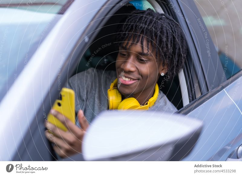 Schwarzer männlicher Fahrer, der im Auto mit seinem Smartphone spricht Mann PKW offen benutzend Streetstyle cool Telefonanruf Stil Kommunizieren Anschluss Gerät