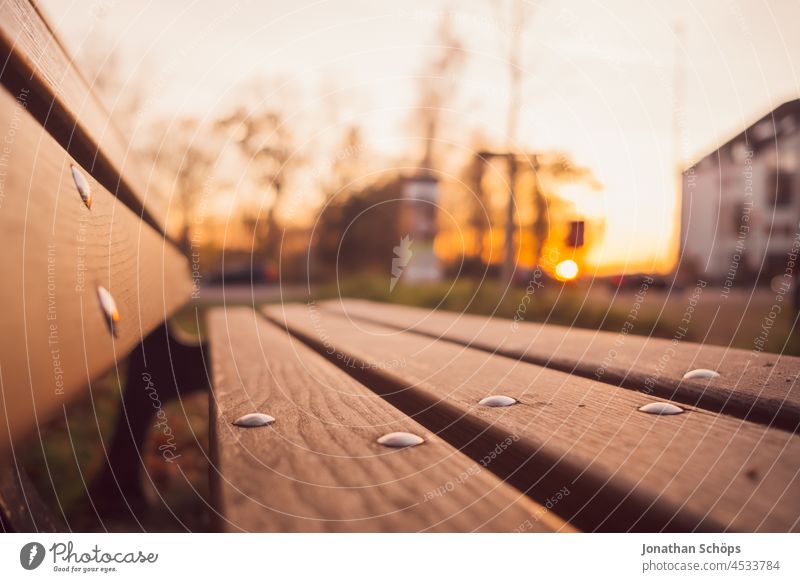 Parkbank an Straße bei Sonnenuntergang im Herbst abend Abendlicht Sitzbank Holzbank Weitwinkel Nahaufnahme braun orange warme Farben Außenaufnahme Farbfoto Bank