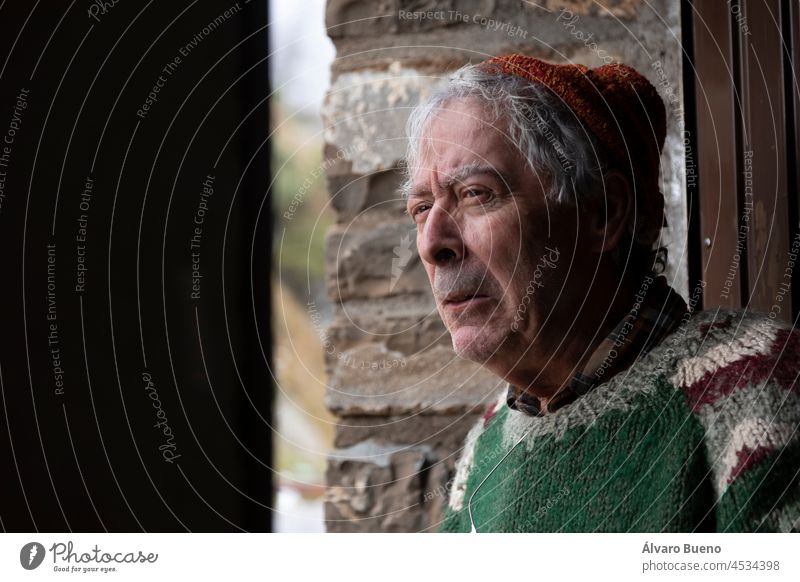 Ein Bergsteiger, älterer erwachsener Mann in den 70ern, mit handgefertigtem Wollpullover, beobachtet die Umgebung von der Tür einer Berghütte aus, Pyrenäen, Spanien