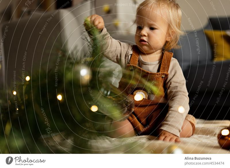 Lifestyle-Porträt von niedlichen kaukasischen Baby ein Jahr alt spielen mit Tannenbaum auf dem Boden zu Hause. Frohe Weihnachten und ein gutes neues Jahr 2022