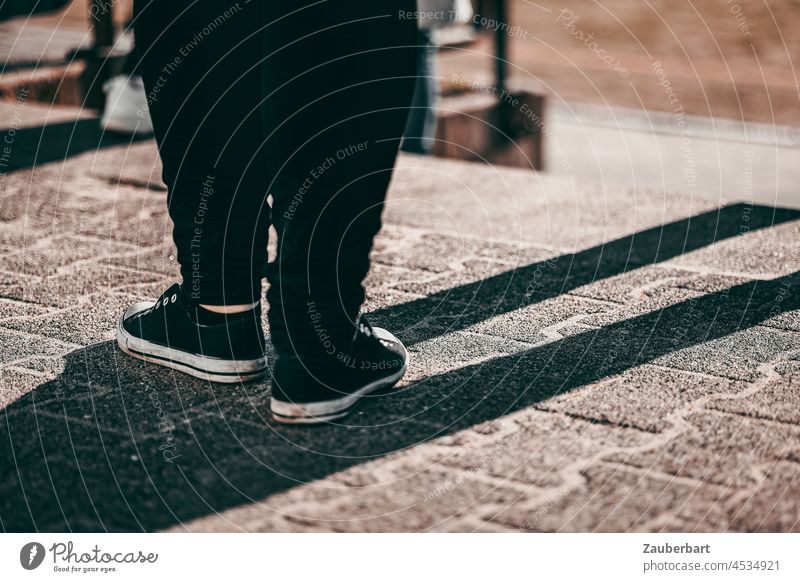 Schwarze Hose, Sneaker, Beine stehen mit Schatten auf Pflaster Standbein Spielbein dick Platz Schuhe schwarz Fuß warten Turnschuh Bekleidung Jugendlich casual