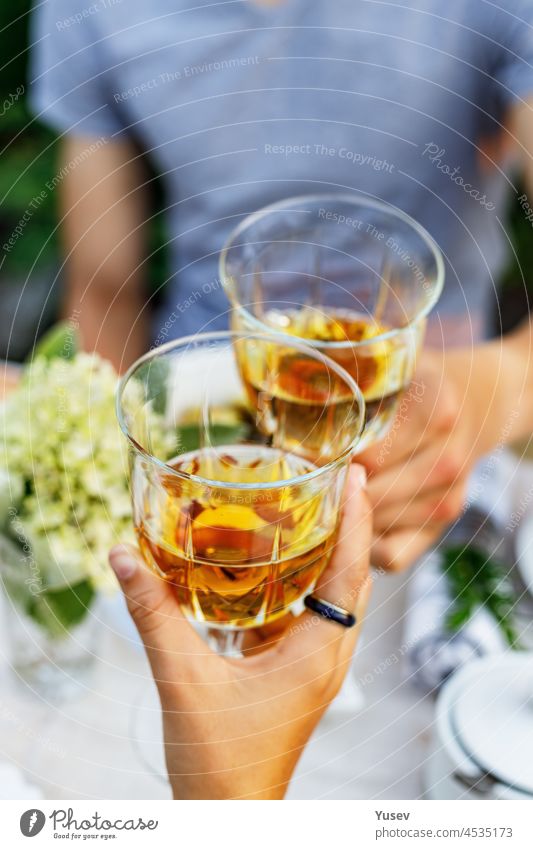 Eine glückliche Familie, die bei einem sommerlichen Gartenfest zu Abend isst und auf die Getränke anstößt. Es wird angestoßen und getrunken. Festliches Familienessen im Hinterhof. Männliche und weibliche Hände halten Gläser mit Wein. Lebensstil