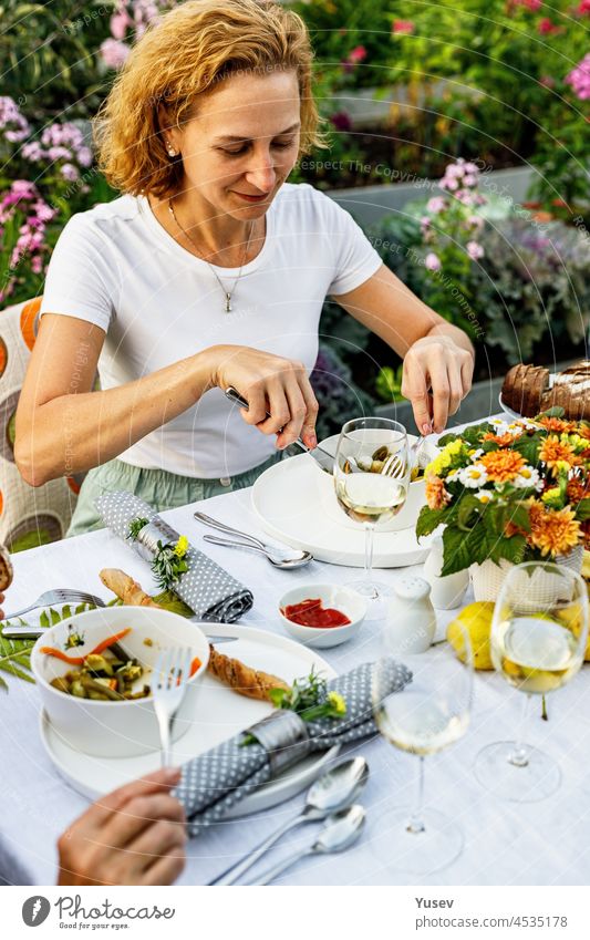 Glückliche Familie bei einem festlichen Abendessen oder Grillfest im Sommergarten. Junge schöne Frau essen köstliche Grill Fleisch und Gemüse. Familie Abendessen in den Hinterhof Konzept. Lebensstil