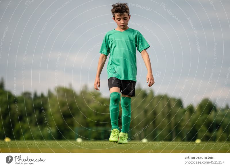 Junger Fußballspieler in Sportkleidung geht nachdenklich auf Fussballplatz junge Fußballplatz Fußballtraining Fußballfeld Fußballschuhe Fußballer sportlich