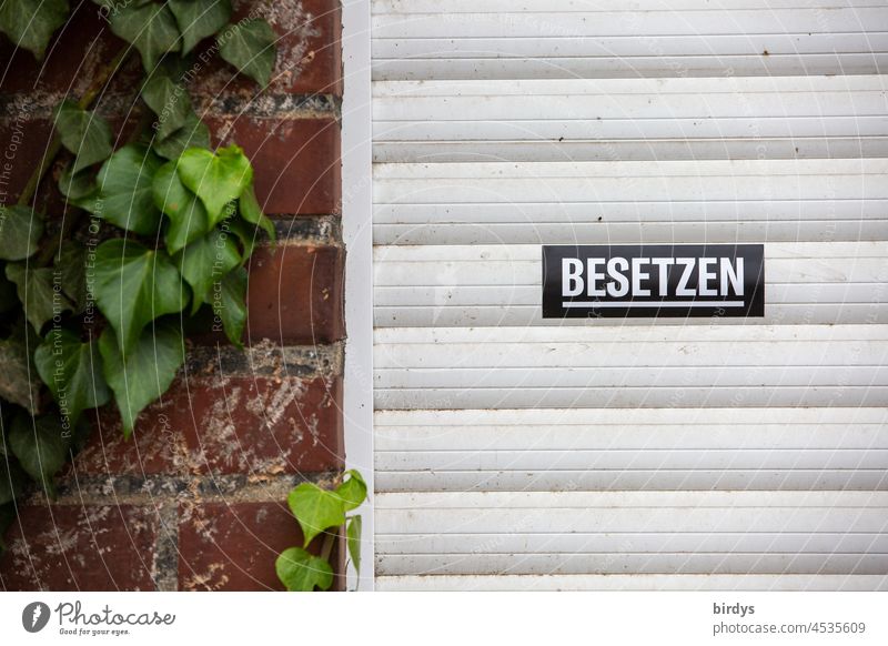 Leerstehendes Haus , herunter gelassener Rollladen mit einem Aufkleber und der Aufforderung das Haus zu besetzen. Leerstand Immobilie Spekulation Hausbesetzung