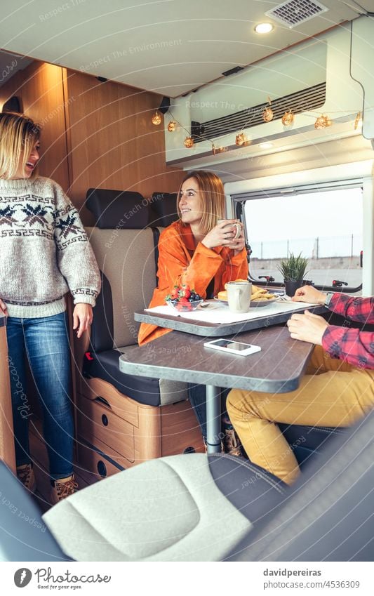 Freunde beim morgendlichen Frühstück im Wohnmobil Frauen trinken Frucht Kaffee Lächeln Brötchen Tisch Blaubeeren Erdbeeren Wohnwagen Kleintransporter Glück