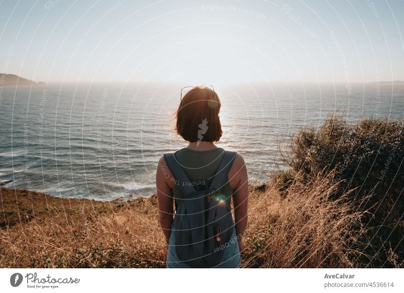 Zurück Bild eines jungen Rucksack-Reisenden Wanderer während einer atemberaubenden Sonnenuntergang Küstenlinie Szenario, Hipster-Reisende Konzept, Schönheit Landschaft. Kopierraum für Text. Bewegung und Freiheit, Nomadenleben.