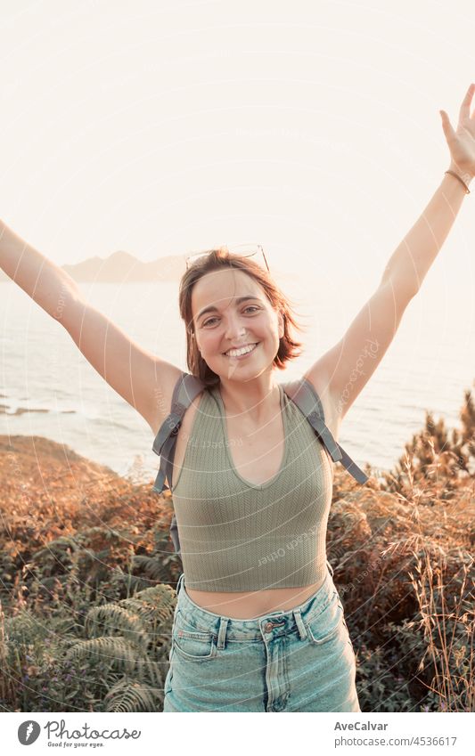 Junge Rucksack Mädchen Reisende feiern Erreichen seines Ziels Wanderer während einer atemberaubenden Sonnenuntergang Küstenlinie Szenario, Hipster Reisende Konzept, Schönheit Landschaft. Bewegung und Freiheit, Nomadenleben.