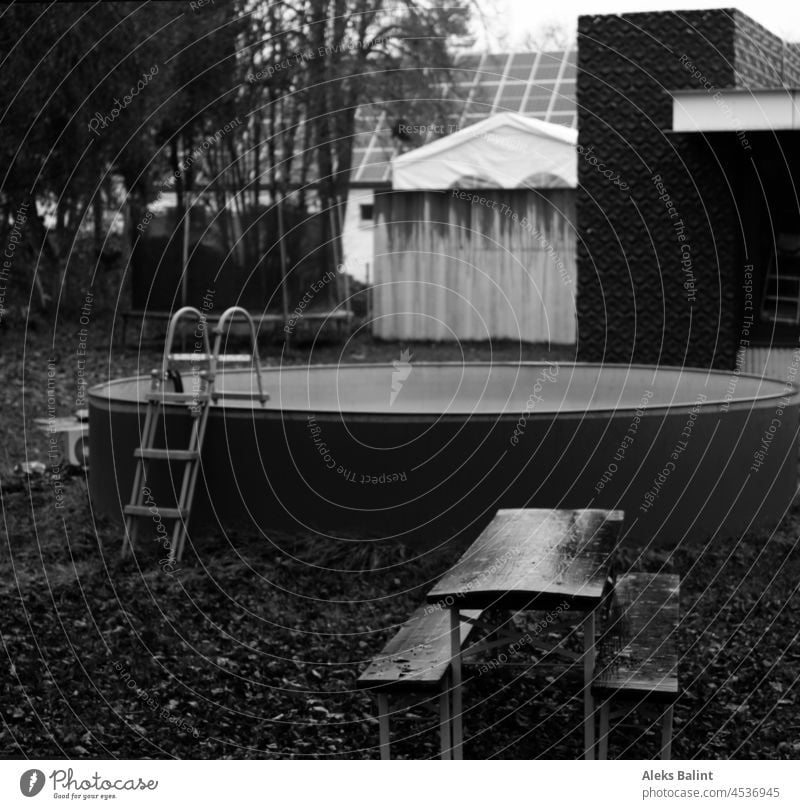 Verlassener Garten im Herbst mit leerem Pool, Tisch und Bänken im Regen und Laub. Tischundbänke nass Menschenleer Außenaufnahme herbstlich Vergänglichkeit