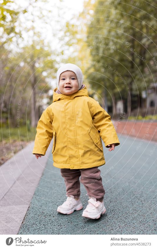 Cute kaukasischen Baby Mädchen ein Jahr alt zu Fuß im Herbst im Freien. Glückliche gesunde Kind mit Smiley-Gesicht genießen das Leben und Herbst Saison auf Sonnenuntergang