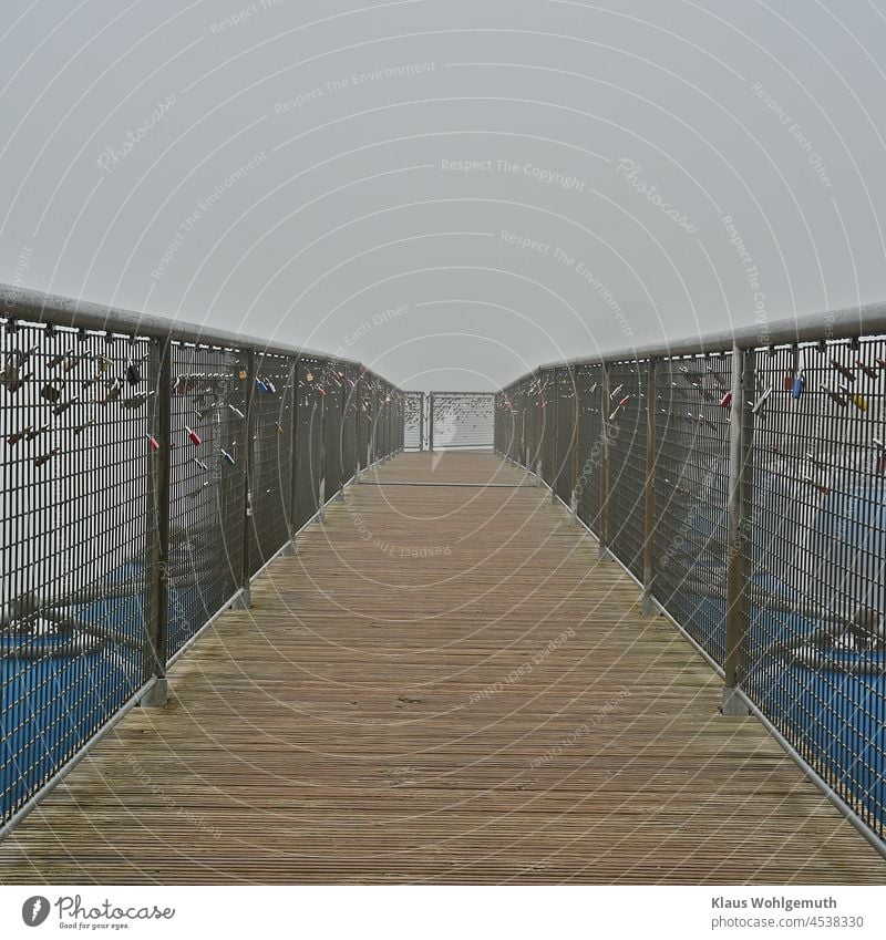 Pontonbrücke im Novembernebel, mit "Liebesschlössern" an den Geländern Brücke Nebel Herbst Vorhängeschlösser Bohlen Holz Metallzaun Perspektive blau grau gelb