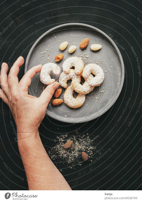 Eine Hand greift nach einem Vanillekipferl auf einem Teller Keks Weihnachten & Advent greifen backen Plätzchen Weihnachtsgebäck süß rustikal Servierfertig