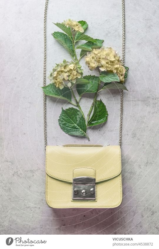 Blassgelbe Frau Handtasche mit Hortensienblüten auf grauem Hintergrund. Feminines Modekonzept mit Blumen. Ansicht von oben. blass feminin Konzept Draufsicht