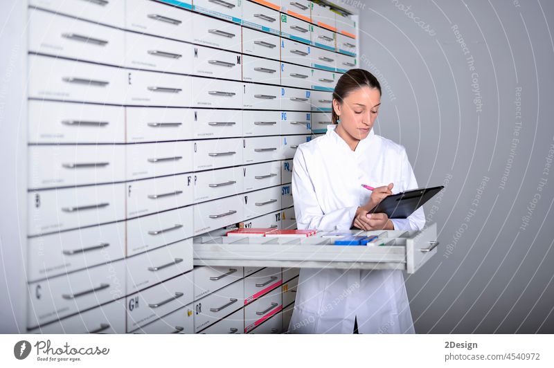 Junge Apothekerin steht neben einem Medikamentenregal und hält eine Tablette in der Hand Uniform Arbeit Gesundheit Medizin Frau hübsch schön 1 Pflege