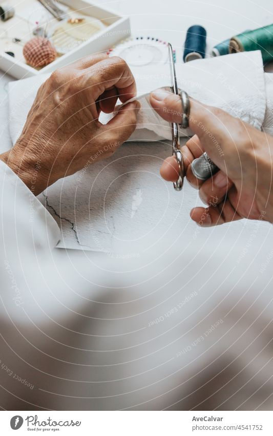 Näherin alte Hände nähen und machen Arbeiten. Stoffarbeiten und Nähen. Lightful Bild, kopieren Raum, Fäden in verschiedenen Farben Hintergrund. Schneiden von Stoff