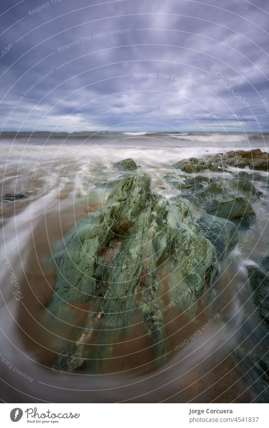 Cullenstown Beach, Wexford, Irland. Spektakuläre Vordergrund voll von sehr mächtigen Felsen mit schönen Linien von Wasser, die es umgeben. Sehr bewölkter Himmel mit leichten Lichtausbrüchen.