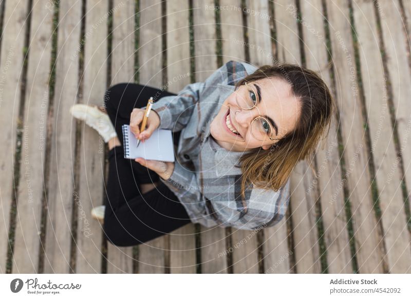 Verträumte Frau sitzt auf der Strandpromenade und schreibt in ein Notizbuch in der Natur zur Kenntnis nehmen Notebook Weg Lächeln schreiben verträumt