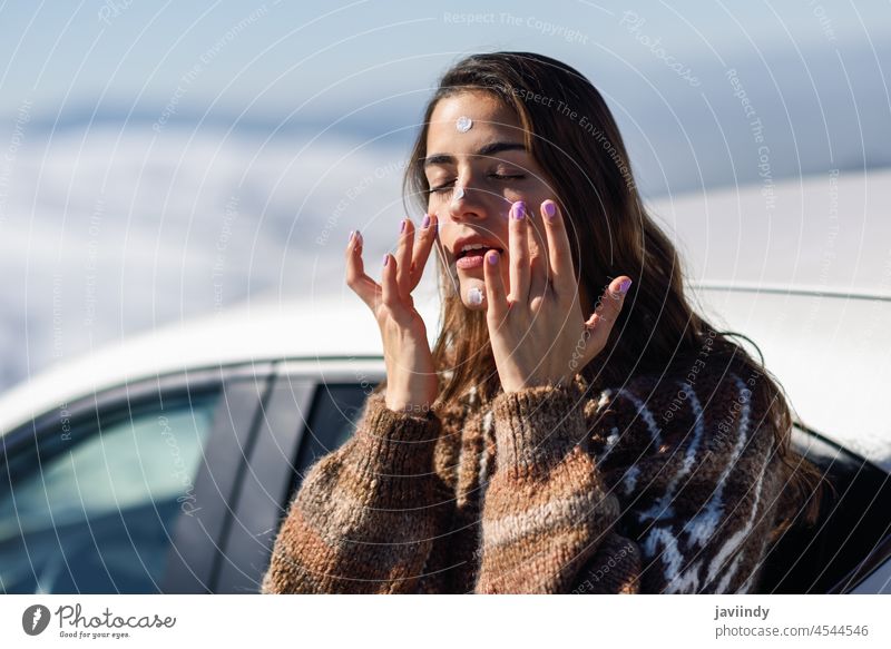 Junge Frau trägt in einer Schneelandschaft Sonnenschutzmittel auf ihr Gesicht auf Sahne Sonnencreme Berge u. Gebirge Winter Lotion Pullover Natur Pflege Schutz