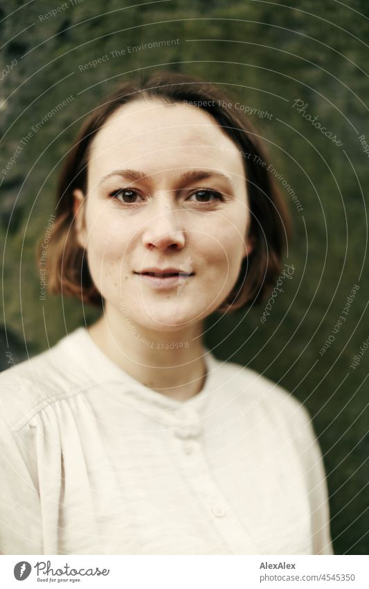 Portrait einer jungen Frau im Park im Herbst vor einer Natursteinwand heiter Leichtigkeit beige grün schönes Wetter Stimmung Frauengesicht Gesicht Freizeit