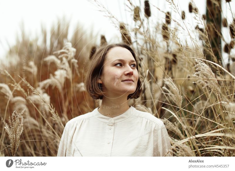 Portrait einer jungen, lächelnden Frau im Park im Herbst vor trockenen Gräsern heiter Leichtigkeit beige grün schönes Wetter Stimmung Frauengesicht Gesicht