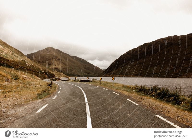 Eine leere Landstraße und eine atemberaubende Landschaft in Irland. Berge, Hügel und ein See neben der Straße. Berge u. Gebirge reisen Himmel malerisch Asphalt