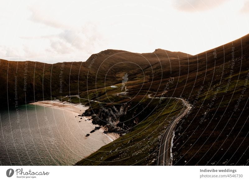 Ein schöner Sonnenuntergang am Meer. Eine ruhige Bucht mit Bergen im Hintergrund. Leere Straße, Drohnenfotografie. Berge u. Gebirge Republik Irland Landschaft