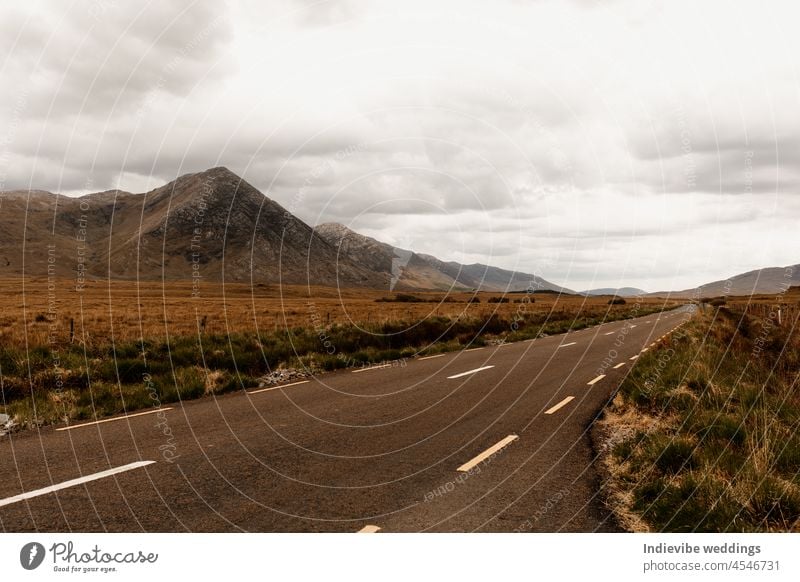 Leere Straße in Irland. Herbst in Connemara. Bedeckter Tag mit Wolken, Bergen und Hügeln. Braunes getrocknetes Gras im Hintergrund. Republik Irland