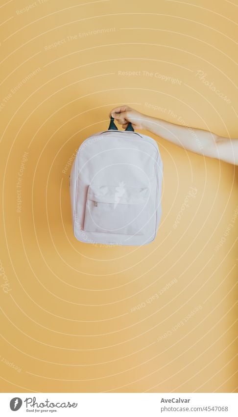 Junge Hand hält rosa Rucksack mit Schulsachen auf gelbem Hintergrund mit Kopie Raum. Zurück zu Schule Konzept Kinder Spielzeug Farben Bildung lehrreich